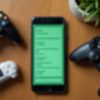 A phone showing a list of apps surrounded by three game controllers on a wooden table